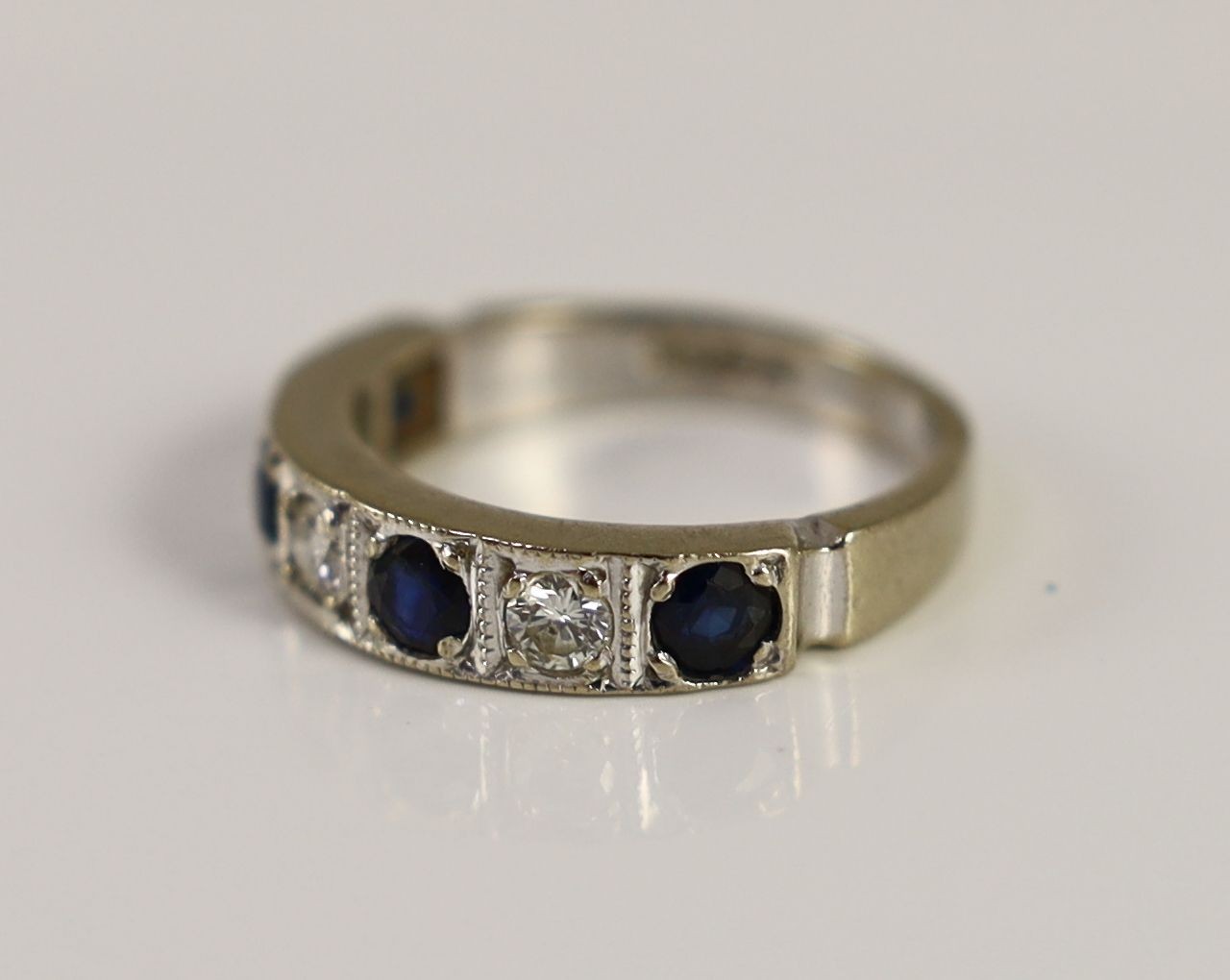 A 1970's 18ct white gold, four stone sapphire and three stone diamond millegrain set half eternity ring